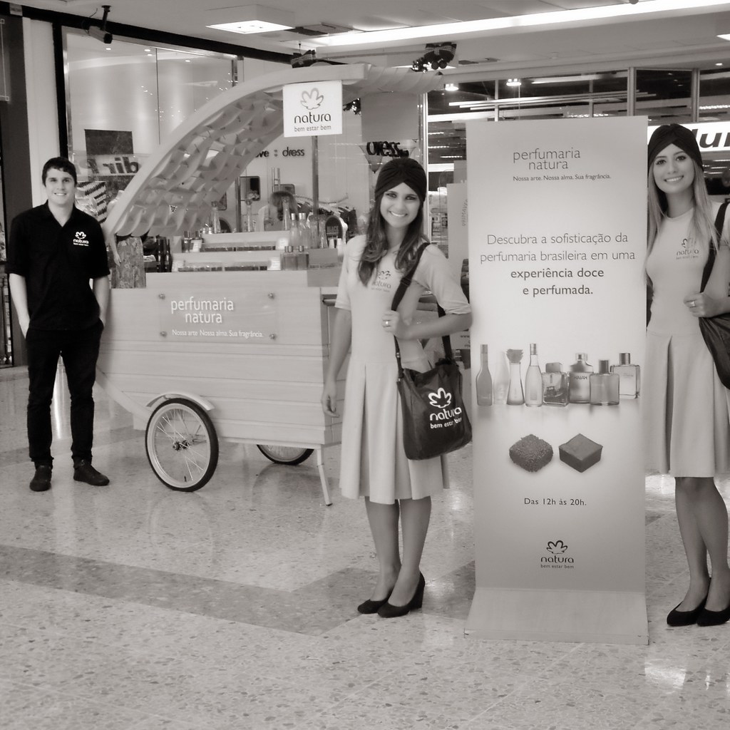 [Imagem de Ação Comercial]: Clientes a interagir com promotoras num stand de shopping em Aracaju.